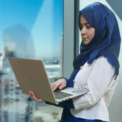 Aliya Shaikh standing with laptop in her hand near a office window